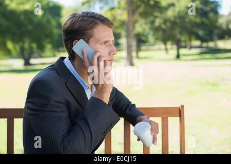 Imprenditore Casual parlando al telefono su una panchina nel parco con caffè Foto Stock