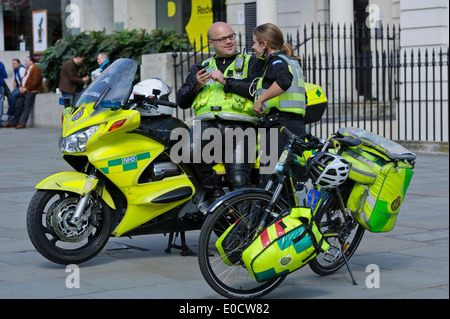 Due paramedici texting sul telefono da una alta velocità di moto e biciclette nella città di Londra, Inghilterra, Regno Unito. Foto Stock