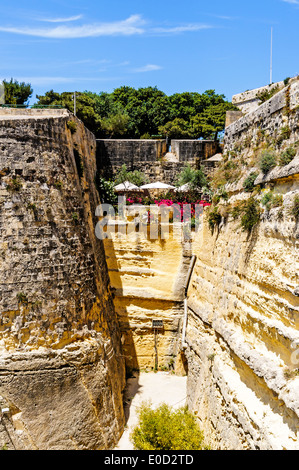 Le imponenti fortificazioni di San Giovanni il bastione e il male weathered cortina muraria che portava alla porta della città di La Valletta, Malta Foto Stock