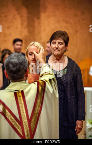 Il parroco di San Timoteo della Chiesa Cattolica, Laguna Niguel, CA, benedice un nuovo membro della congregazione la notte del suo battesimo. Nota sponsor a destra. Foto Stock