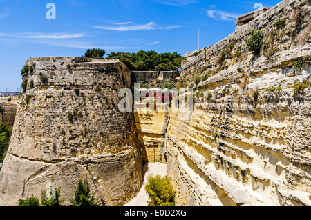 Le imponenti fortificazioni di San Giovanni il bastione e il male weathered cortina muraria che portava alla porta della città di La Valletta, Malta Foto Stock