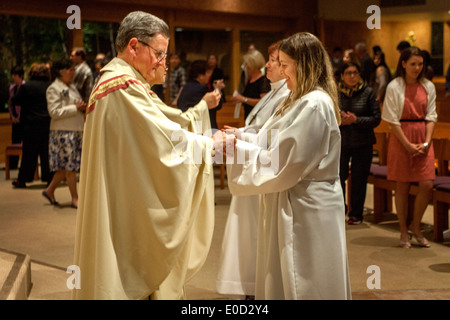 Il parroco di San Timoteo della Chiesa Cattolica, Laguna Niguel, CA, offre la comunione ai nuovi membri della congregazione la notte del loro battesimo. Nota vesti bianche. Foto Stock