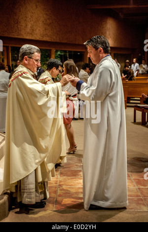 Il parroco di San Timoteo della Chiesa Cattolica, Laguna Niguel, CA, offre la comunione a nuovi membri della congregazione la notte del suo battesimo. Nota vesti bianche. Foto Stock