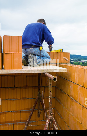 Anonimo lavoratore edile su un sito di costruzione con la costruzione di una casa stabilisce un muro di mattoni. Muro di mattoni di un mas Foto Stock