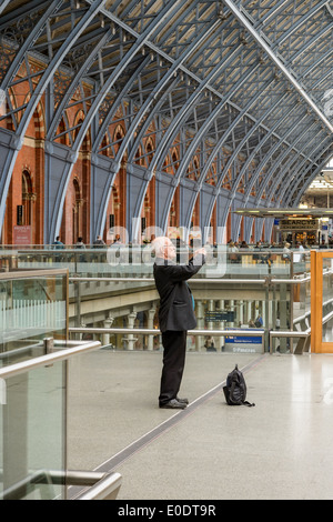 Un uomo prende le foto sul suo videofonino (r nella stazione di St Pancras, London. Smartphone smart phone fotocamera compatta pubblico fotografia Foto Stock