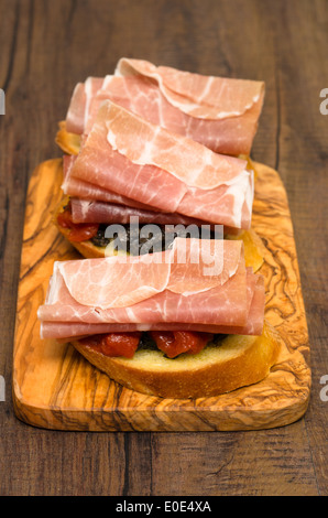 Pane con pasta di olive, pomodori e prosciutto di Parma come snack in formato verticale Foto Stock