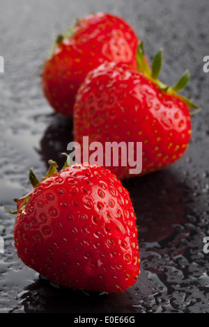 Tre mature intero Fragole organico nero sul tagliere con gocce d'acqua Foto Stock