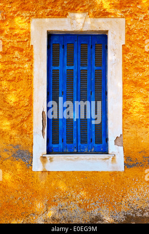 Finestra chiusa con persiane blu degli anziani nella casa gialla parte anteriore Foto Stock