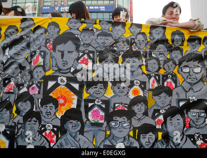 Ansan, Corea del Sud. Il 10 maggio 2014. Le persone che frequentano un rally di fronte appeso un quadro raffigurante le vittime del traghetto Sewol e dei loro familiari a plaza, Ansan, Corea del Sud, di sabato 10 maggio, 2014. Il rally è stato tenuto contro che cosa esse insistono, lax risposta del Presidente Parco-geun hye il governo dopo il traghetto Sewol è stata affondata nelle acque al largo del sud-ovest di isola Jindo on April 16, 2014. Circa 13.000 persone hanno partecipato al rally per chiedere le dimissioni del Presidente Parco e di cordoglio per le vittime della tragedia, secondo i media locali. Foto Stock