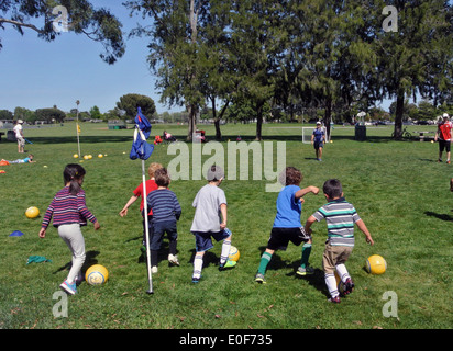 Kids pratica dribbling palla calcio al Summer Camp in posizione di parcheggio Foto Stock