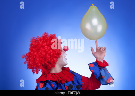 Clown in costume rosso giocare con palloncino giallo su sfondo blu. Studio di illuminazione professionale Foto Stock
