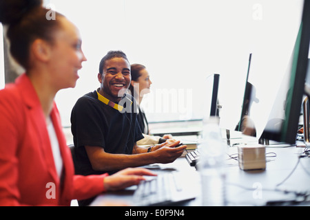 Giovani afro-americano guardando fotocamera a sorridere mentre si lavora sul computer in aula moderna. I giovani studenti. Foto Stock