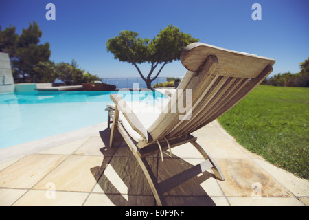 Lungo sedia a sdraio a bordo piscina. Vuoto lounge in legno sedia accanto alla piscina al centro di villeggiatura. Foto Stock