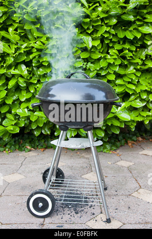 Vecchio nero barbecue utilizzato, il fumo proveniente dalla parte superiore Foto Stock