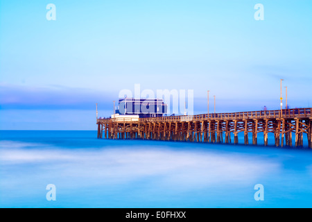 Balboa pier a Newport Beach in California durante il sunrise mostra la struttura di legno del molo e un vibrante, il blu del cielo e del mare. Foto Stock