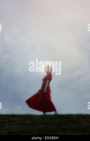 Una ragazza in un abito rosso sta ballando su un prato Foto Stock