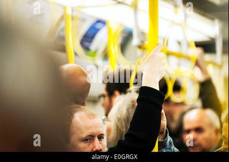 Un " commuter " tenuta su di un post su un affollato Londra della metropolitana treno. Foto Stock