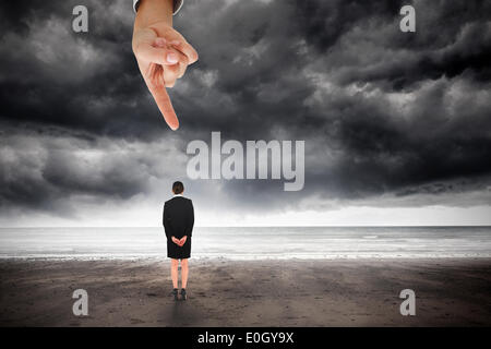 Mano gigante puntando al giovane imprenditrice in piedi con le mani dietro la schiena Foto Stock