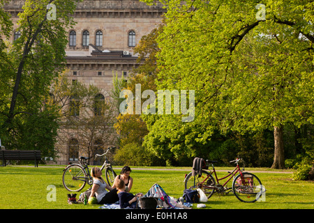 Giovani rilassante su un parco Prato, teatro di Stato in background, Brunswick, Bassa Sassonia, Germania Foto Stock