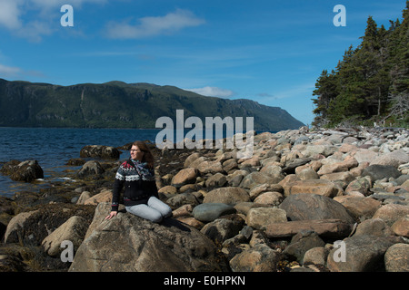 Donna seduta sulle rocce a costa, Norris punto, Bonne Bay, Parco Nazionale Gros Morne, Terranova e Labrador, Canada Foto Stock