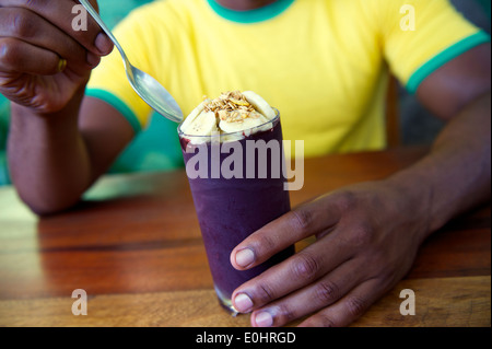 Uomo brasiliano in Brasile colori shirt mangiare una tazza di carni congelate acai acai con banana Foto Stock