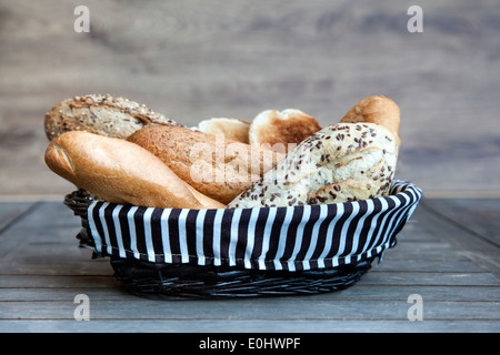Un assortimento di pane in un cestino in un rustico sfondo di legno Foto Stock