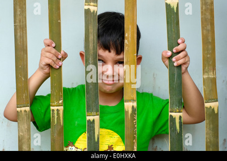 Giovane ragazzo locale del peering attraverso un recinto di bambù in Giava Est Indonesia Foto Stock