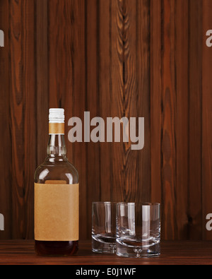 Due bicchieri con ghiaccio per whiskey e bottiglia sul legno scuro dello sfondo. Foto Stock