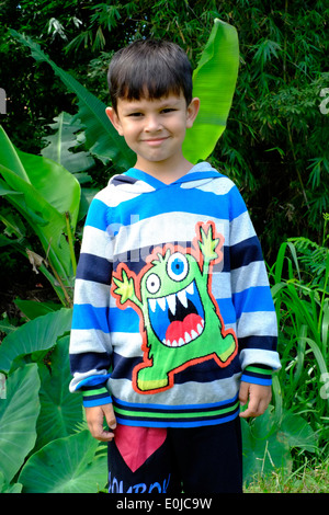 Little Boy giocando da solo mentre indossa con fierezza il suo nuovo mostro alto in un villaggio rurale in Giava Est Indonesia Foto Stock