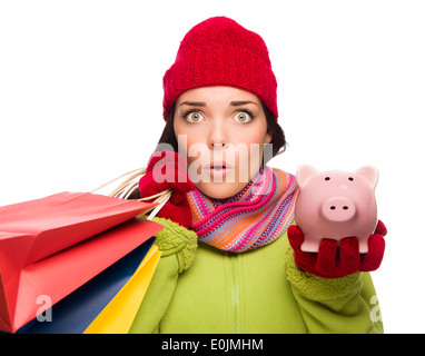In questione razza mista donna che indossa abiti invernali, tenendo le borse della spesa e Piggybank isolati su sfondo bianco. Foto Stock