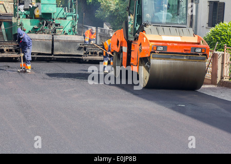 Lavoratori, rullo operativo e di asfalto lastricatore macchina durante la costruzione di strade e lavori di riparazione Foto Stock