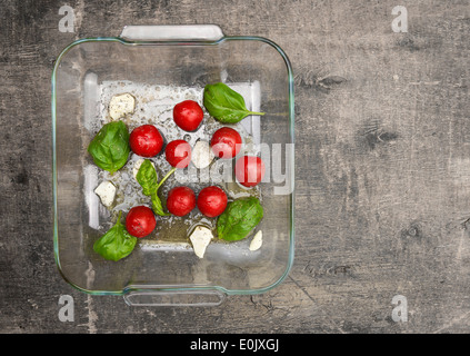 Pomodori con basilico e aglio in vasca in vetro su legno antico, la preparazione per la tostatura, vista dall'alto Foto Stock