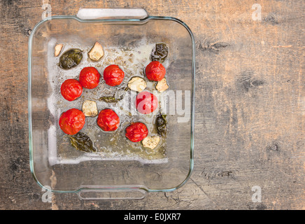 Arrosto di pomodori ciliegia in vetro con basilico e aglio sul tavolo di legno Foto Stock