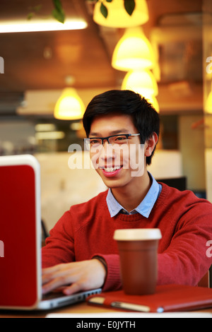 Sorridente uomo asiatico in bicchieri lavorando sul computer portatile in ufficio Foto Stock