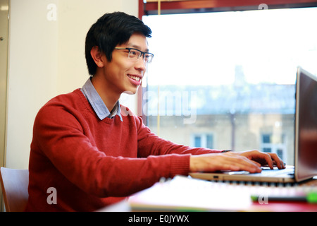 Sorridente uomo asiatico in bicchieri lavorando sul computer portatile in ufficio Foto Stock