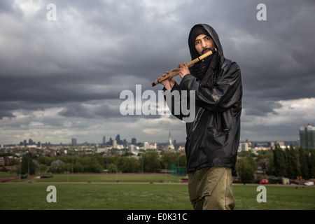 Razza mista uomo suonare il flauto in erba lunga su Hampstead Heath indossa velo e nero camicia lucida Foto Stock