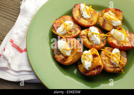 Una piastra di grigliate di pesche con creme fraiche, guarnita con bucce di arancia, rosmarino tritato e aceto balsamico. Foto Stock