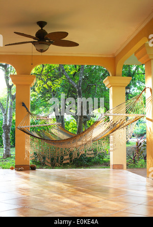 Un invitante amaca appesa su un soleggiato portico con i tropici in background. Foto Stock