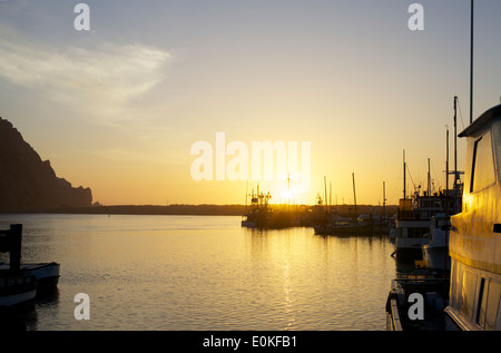 Barche di galleggiare sull'acqua come il sole tramonta sull'orizzonte a Morro Bay, California. Foto Stock