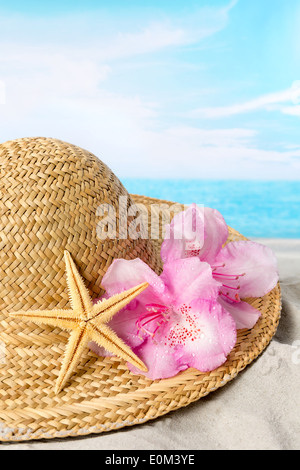 Cappello per il sole con fiori di colore rosa e la stella di mare sulla spiaggia Foto Stock