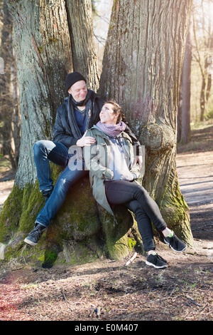 Coppia felice in natura l'impostazione. Giovane uomo e donna seduta da un albero, riposo durante una passeggiata nei boschi. Foto Stock