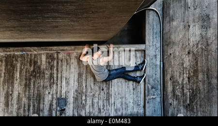 Giovane uomo appeso in una parkour spostare sul muro di cemento scena urbana con il momento dello stile di vita dei giovani pieni di energia e forza Foto Stock