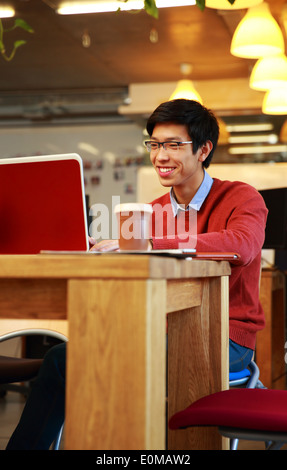 Sorridente uomo asiatico in bicchieri lavorando sul computer portatile Foto Stock