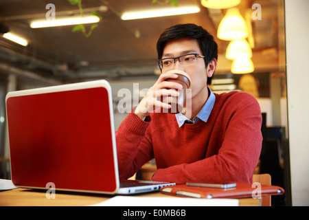 Bel uomo asiatico lavorando su laptop e di bere il caffè Foto Stock