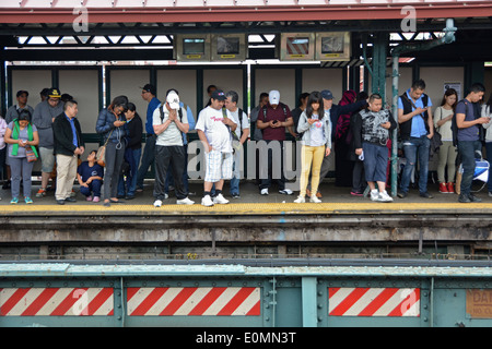 Pendolari, molti con telefoni cellulari, sulla 74a Strada piattaforma della metropolitana #7 in treno in Jackson Heights, Queens, a New York Foto Stock