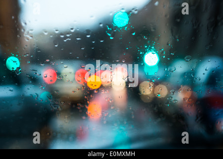 Luce sfocata di vetture visto attraverso un parabrezza bagnato con alcune gocce di pioggia su di esso nella mattina in anticipo di un giorno di pioggia Foto Stock