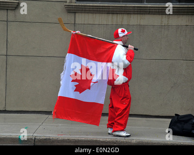 Un uomo canadese tenendo una bandiera canadese e indossa una tuta canadese si erge sul marciapiede. Foto Stock