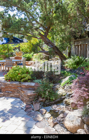 Funzione di acqua corrente che fluisce attraverso la vegetazione lussureggiante nel patio nel bellissimo cortile paesaggistico Foto Stock