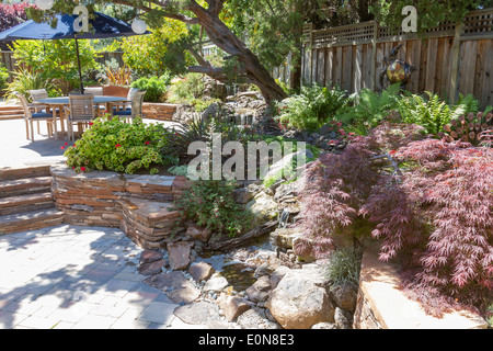 Funzione di acqua corrente che fluisce attraverso la vegetazione lussureggiante nel patio nel bellissimo cortile paesaggistico Foto Stock