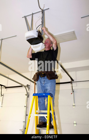 Uomo in piedi su una scala fissaggio meccanico di un dispositivo di apertura garage a distanza Foto Stock